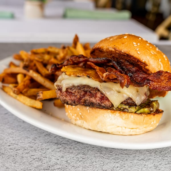 A juicy burger with melted cheese, crispy bacon, and pickles, served with a side of golden fries.