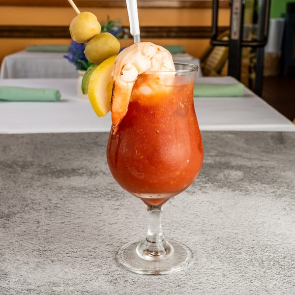 A Tres Palms Bloody Mary cocktail with shrimp, lemon, lime, olives, and a straw.