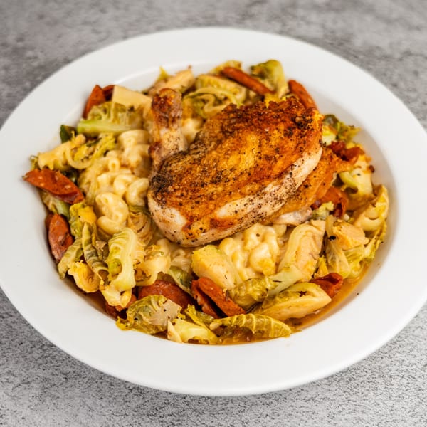 Crispy chicken breast over macaroni and cheese with sautéed cabbage and sliced sausage.