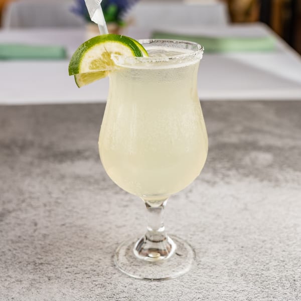 A Tres Palms margarita with a salted rim, lime wedge, and straw on a grey table.