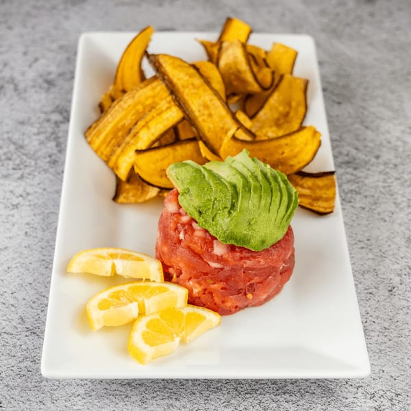 Tres Palms tuna tartare with avocado, lemon wedges, and plantain chips on a white plate.