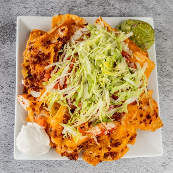 Tres Palms lobster nachos with melted cheese, lettuce, tomato, sour cream, and guacamole.