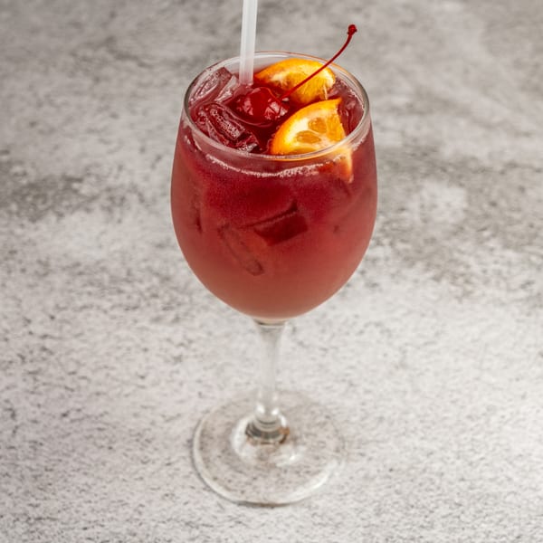 Red sangria cocktail in a wine glass with orange slices, cherries, and a straw.
