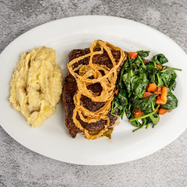 Steak topped with crispy onion rings, served with mashed potatoes and sautéed spinach with carrots.