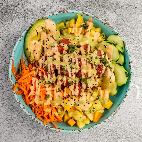 A vibrant poke bowl with tuna, avocado, mango, carrots, and cucumber, drizzled with sauces.