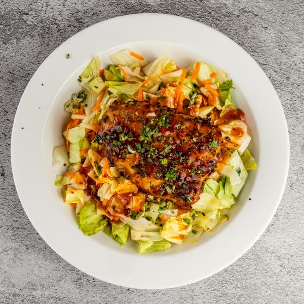 Grilled salmon with a dark glaze and fresh herbs, served on a bed of lettuce and shredded carrots.