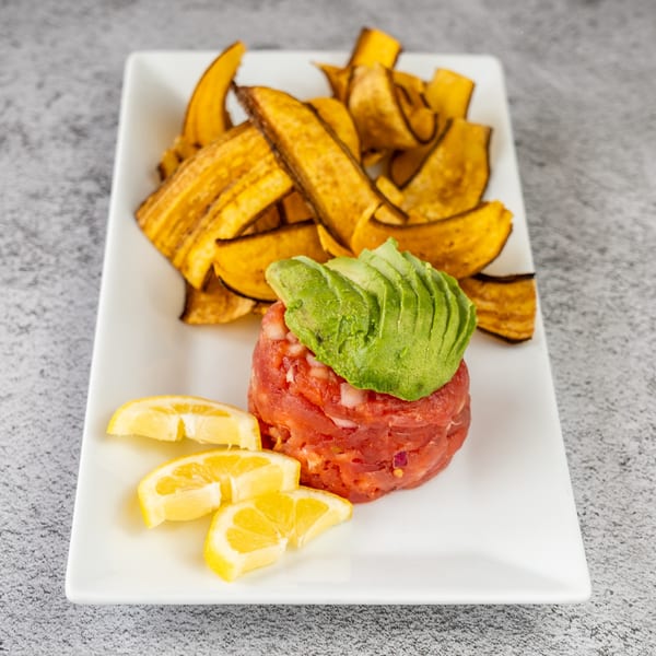 Tuna tartare topped with avocado slices, served with lemon wedges and plantain chips.
